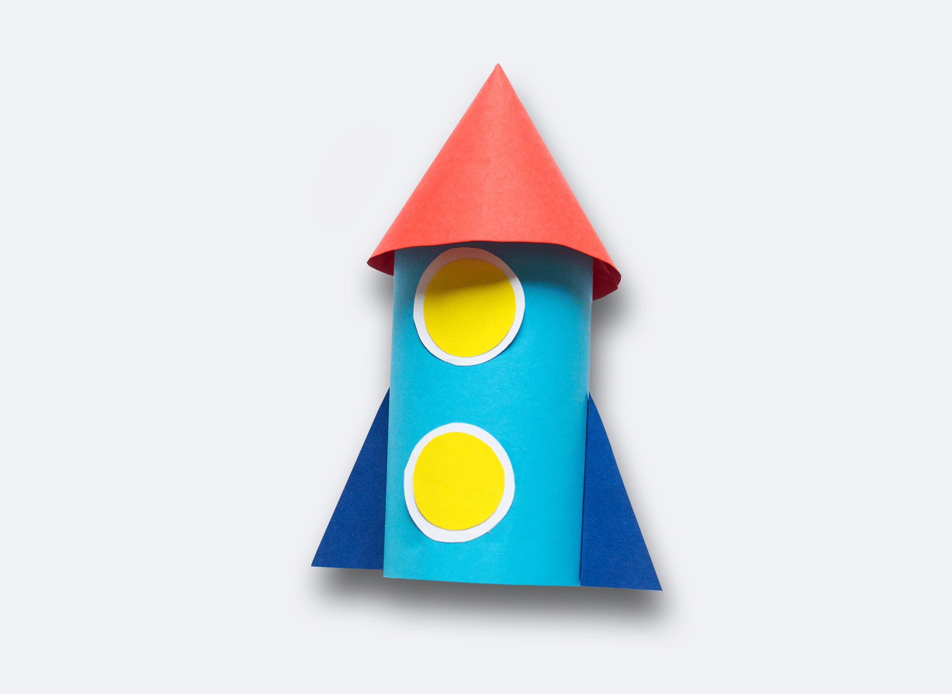 A blue handmade rocket with yellow windows and a red cone. The rocket is made out of a film cannister and construction paper.