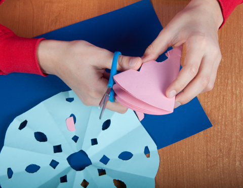 A child's hands cut paper snowflakes