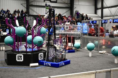 The image is a photograph of a robot with the number 3176 on the base. The robot is standing upright, and is interacting with structure that is populated with large balls.