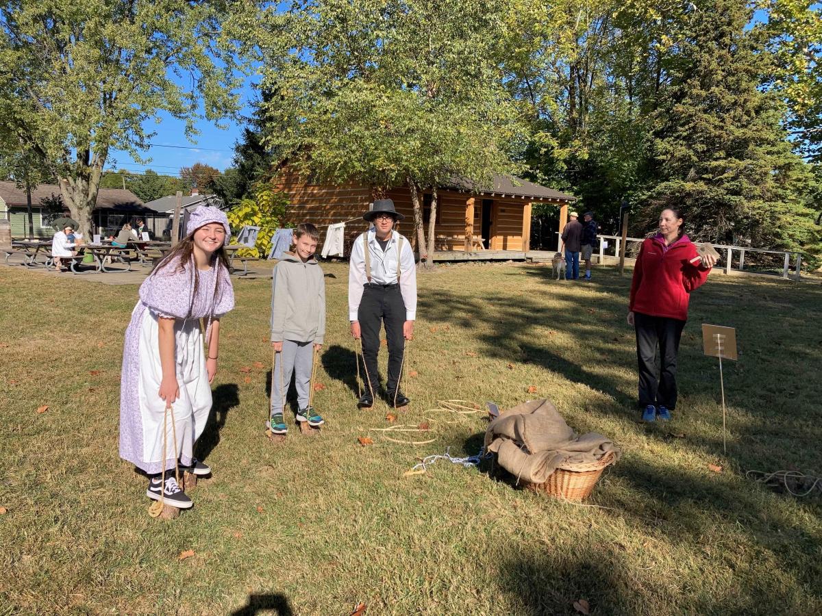 Children in pioneer clothes outside of a log cabin