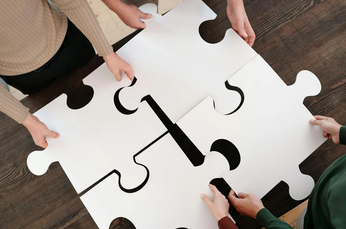 A group of four people holding puzzle pieces and are working on the puzzle together